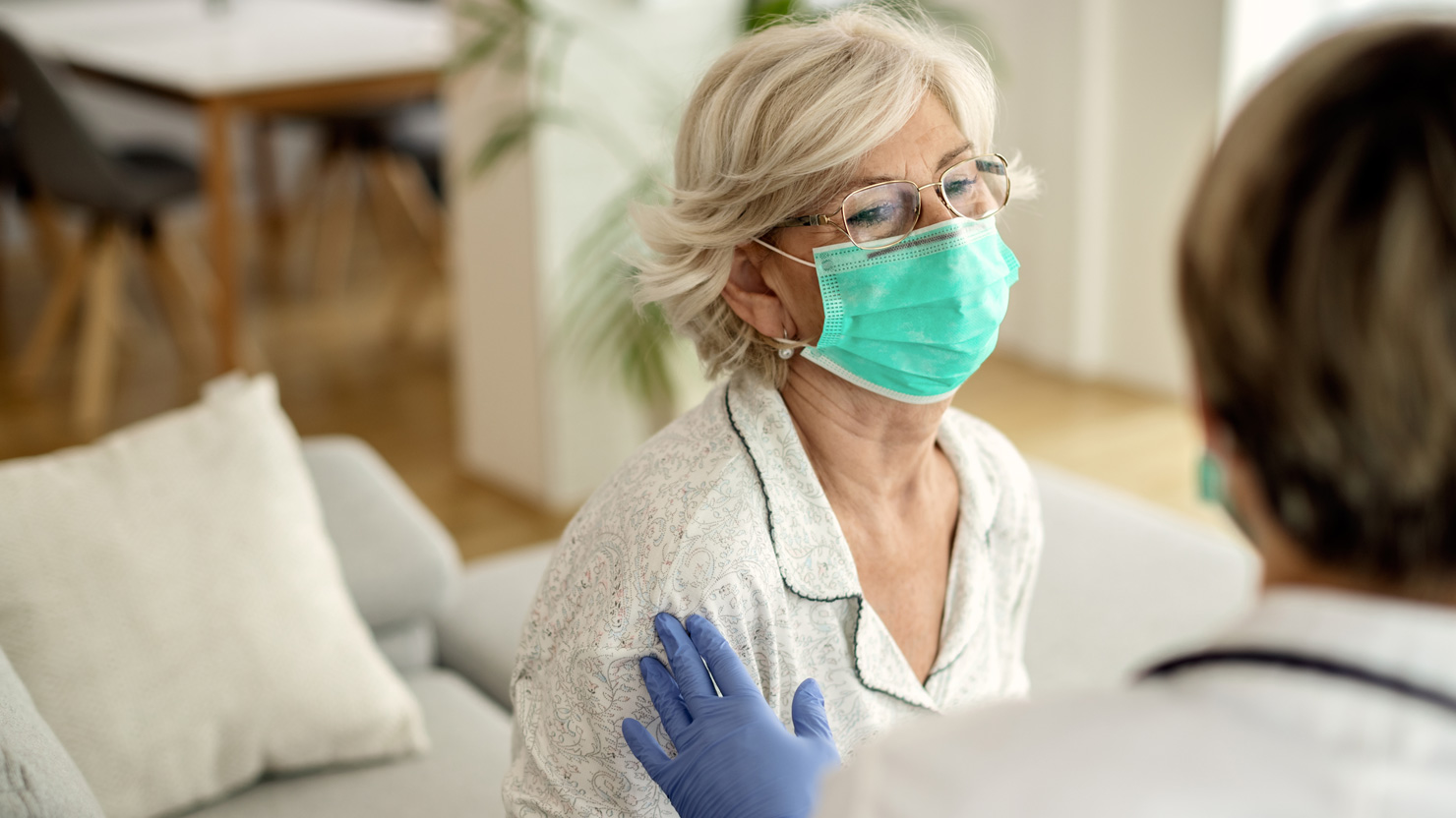 An elderly patient with a surgical mask is visited in her Bay Area home by a mobile phlebotomist for a routine blood draw