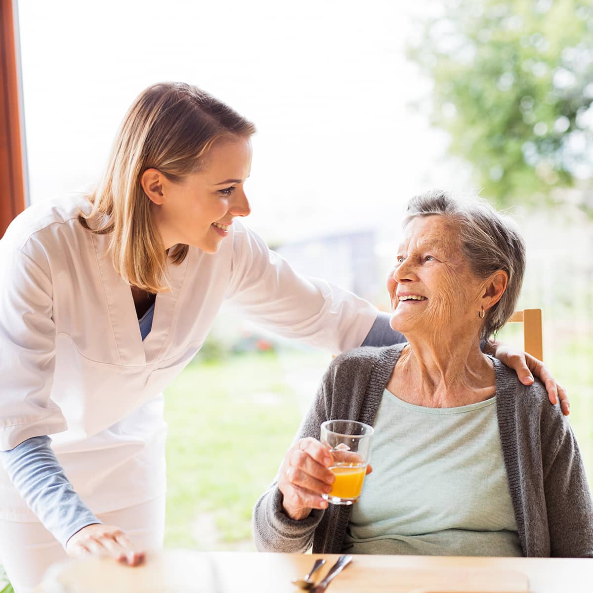 A mobile phlebotomist comforts an elderly woman who is smiling and holding a glass of orange juice